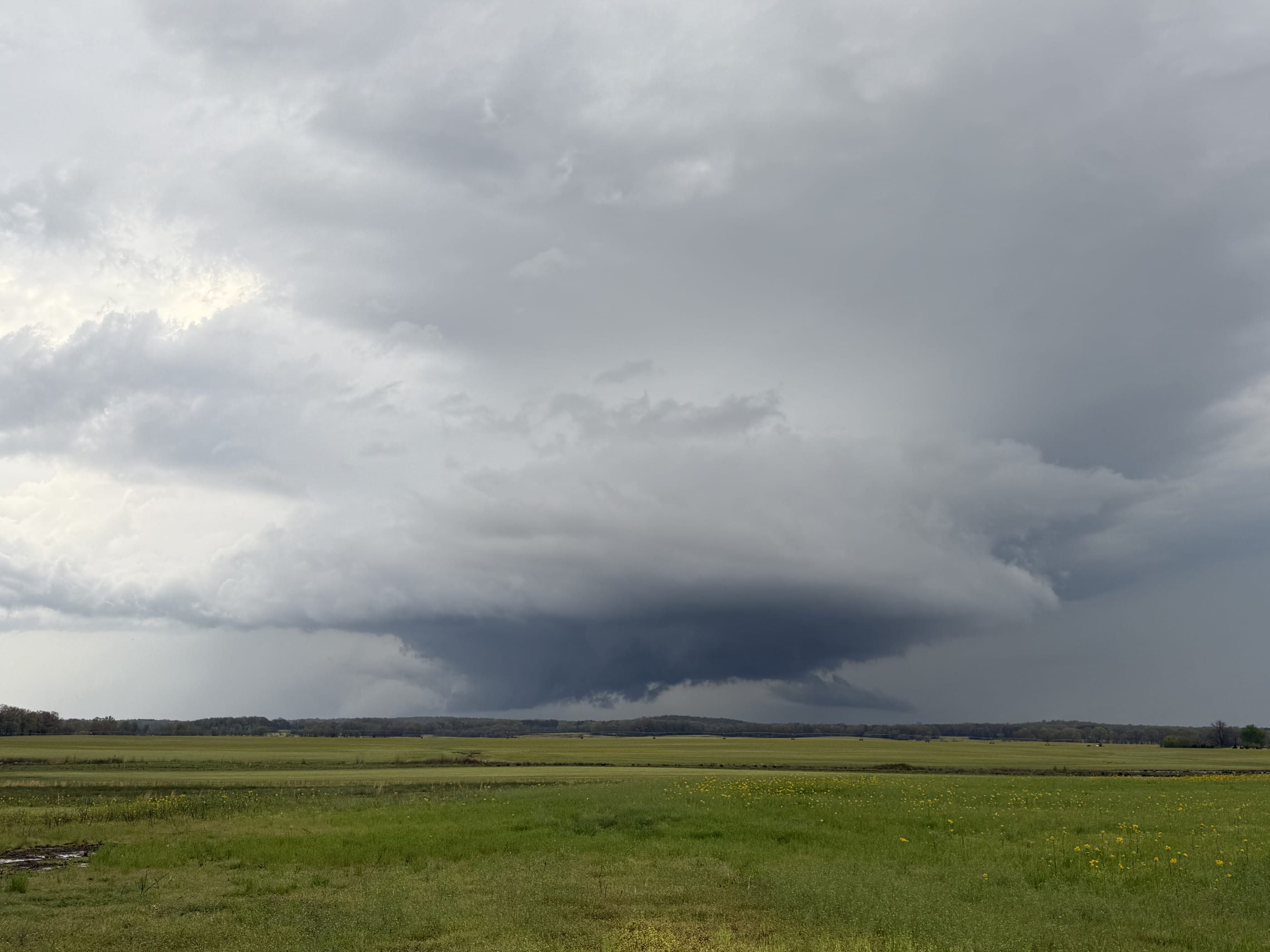 A wide, striated storm base settling over green West Tennessee farmland.