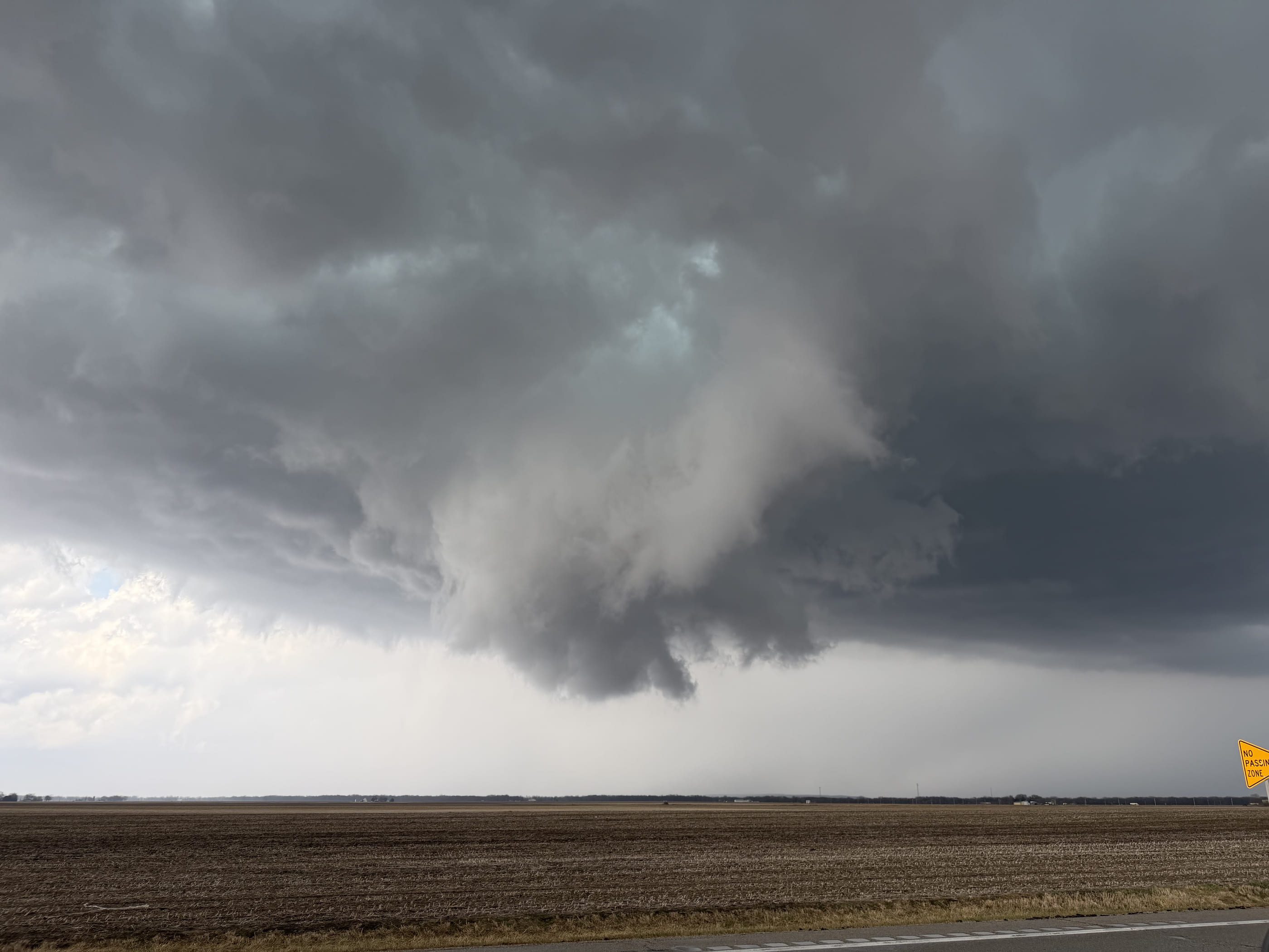 A wall cloud hanging beneath a dark storm base over open farmland near Pontiac, Illinois.